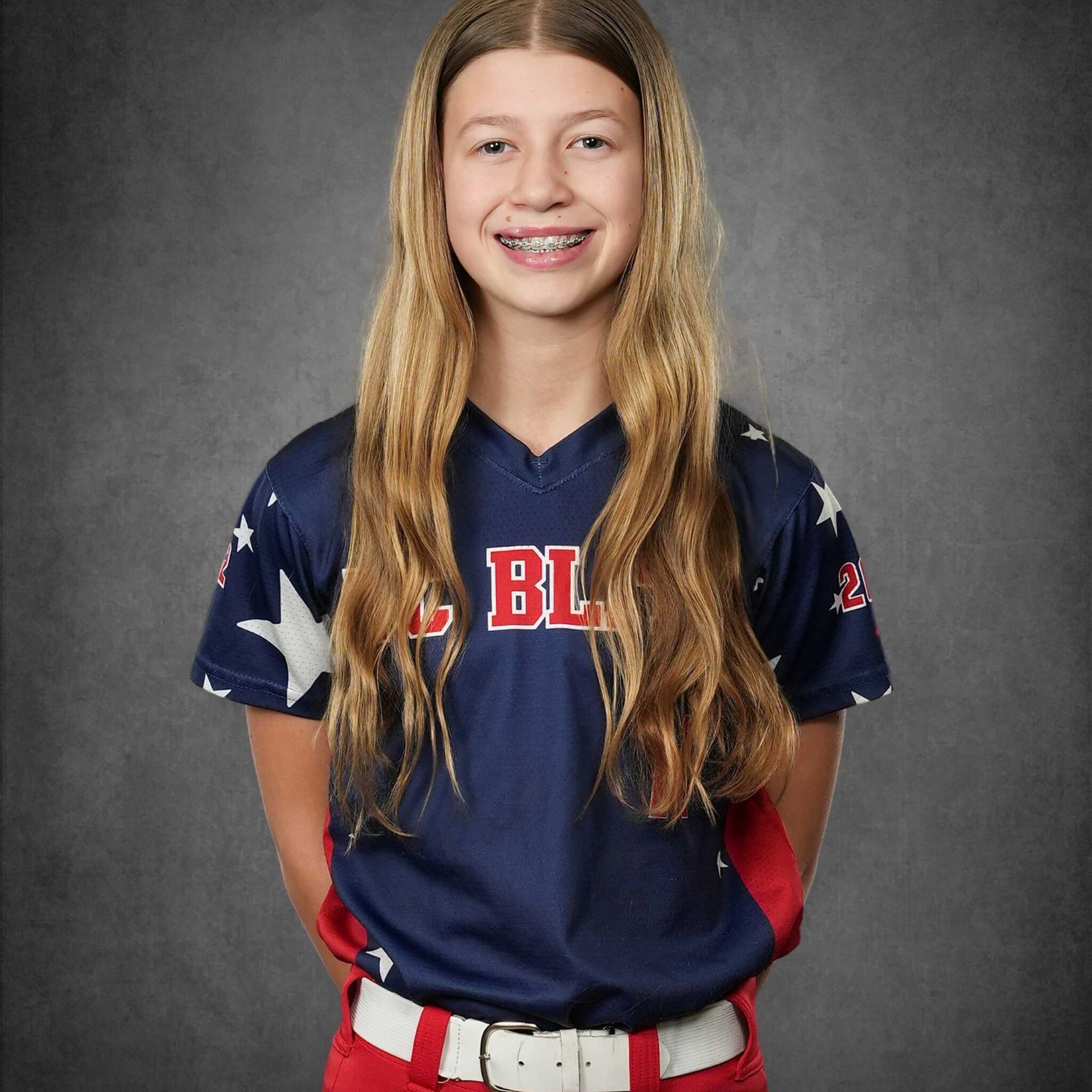 Portrait of a smiling softball player in a navy jersey and red-white pants against a gray backdrop