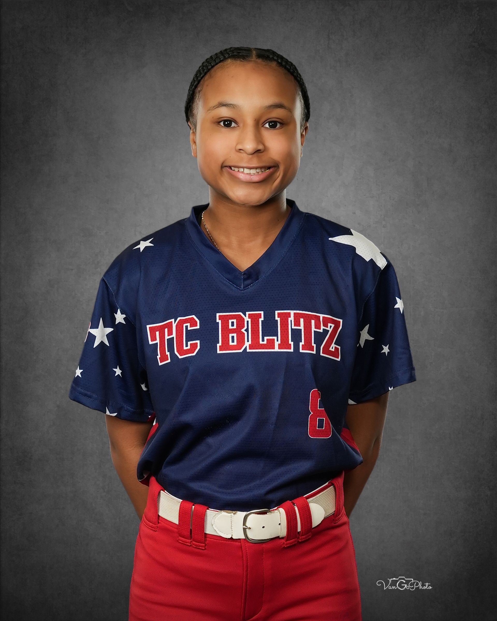 Youth softball player in navy “TC BLITZ” jersey and red pants, standing against a gray studio backdrop.