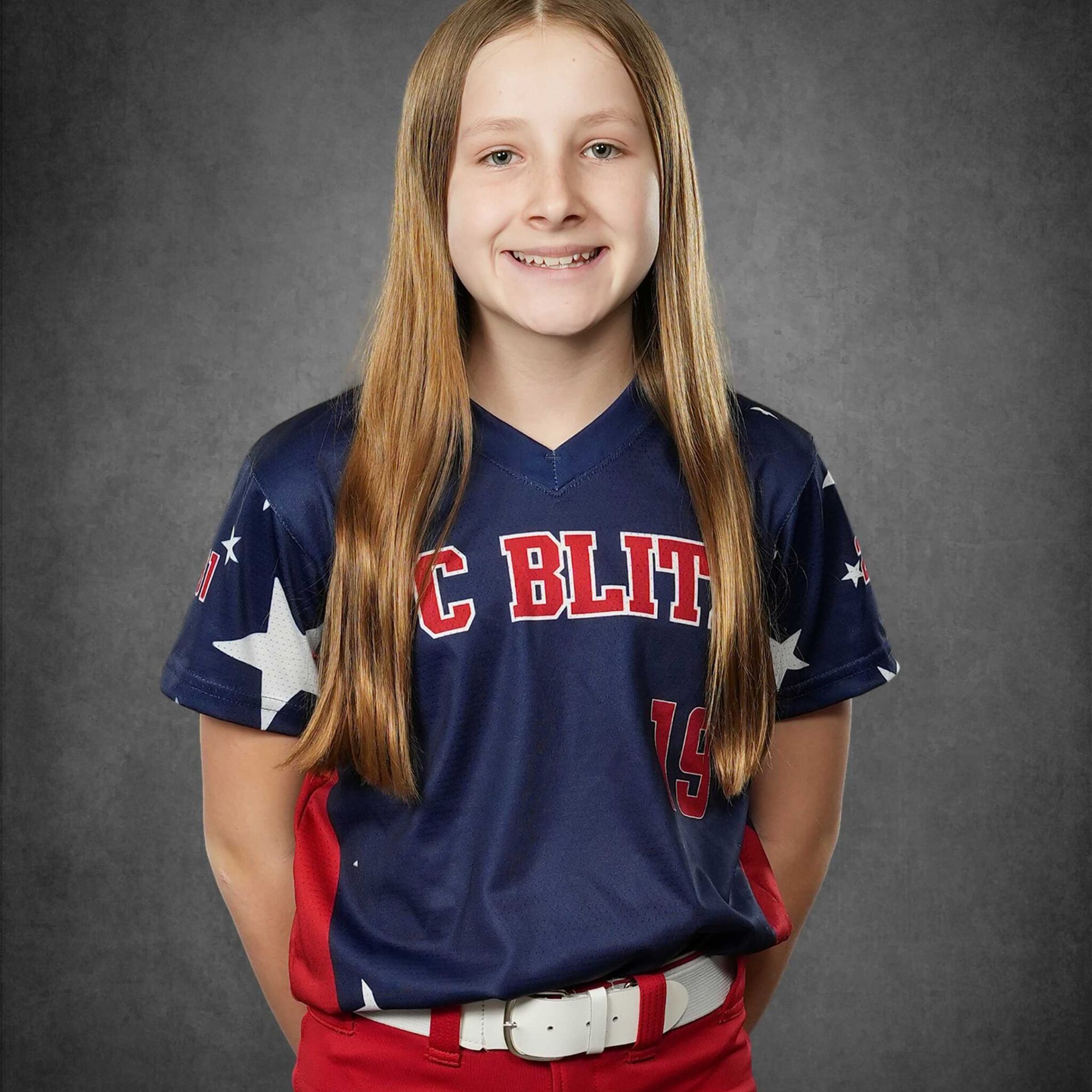 Smiling youth softball player in navy and red uniform against a gray studio backdrop