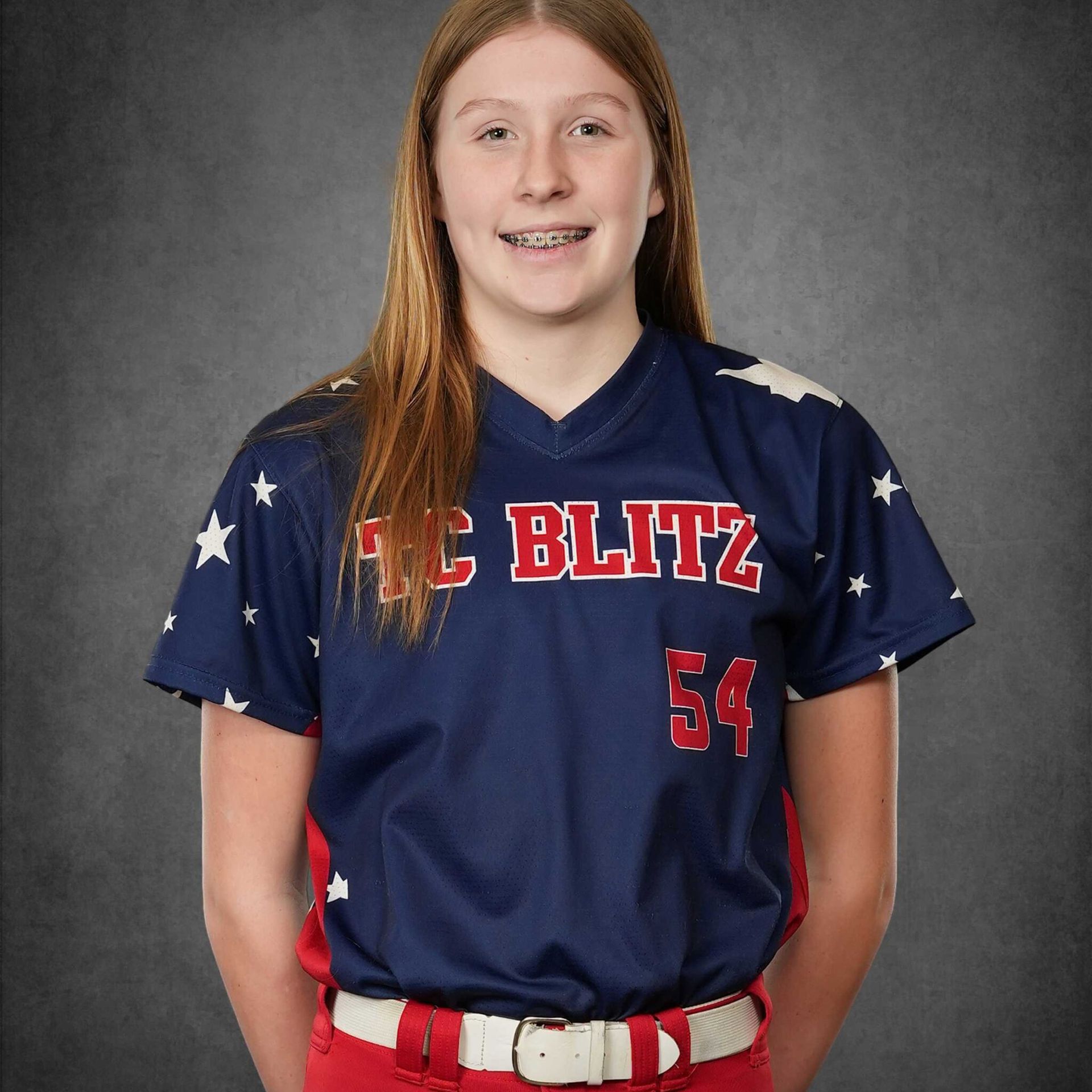 Portrait of a softball player in a navy “PC BLITZ” jersey, smiling against a gray backdrop