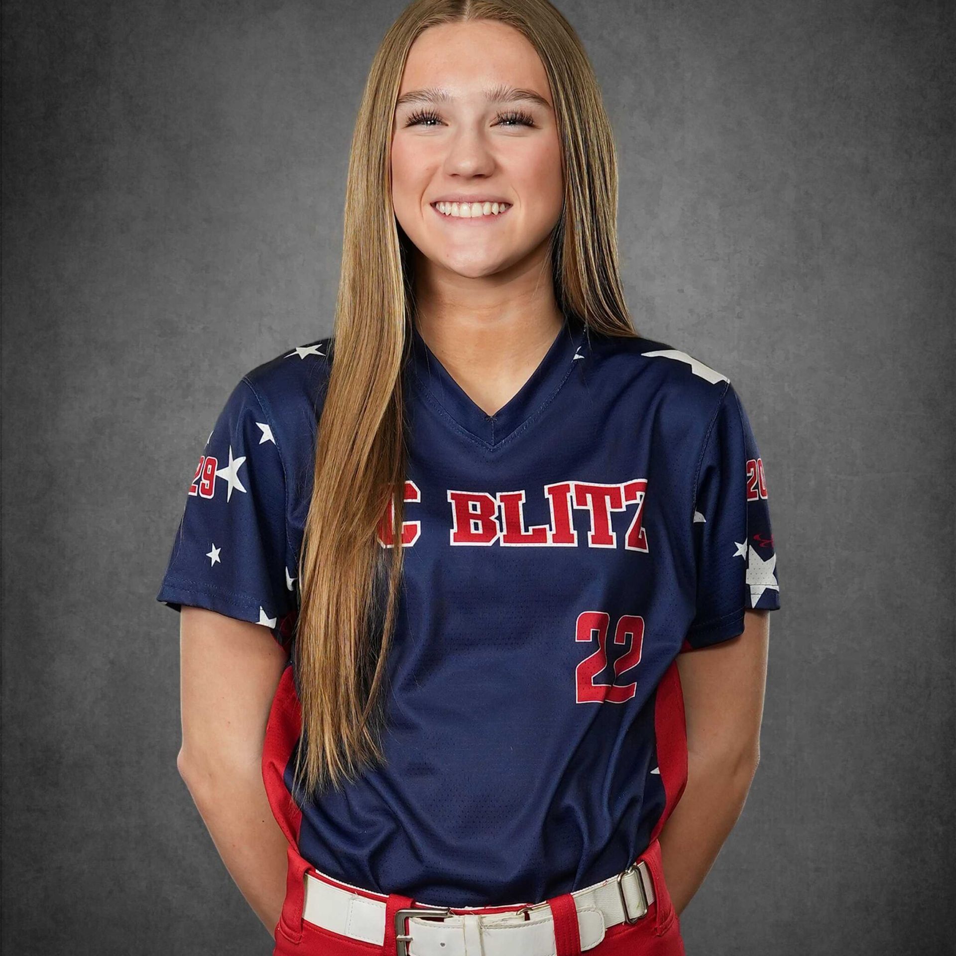 Smiling softball player in navy and red uniform against a gray studio backdrop