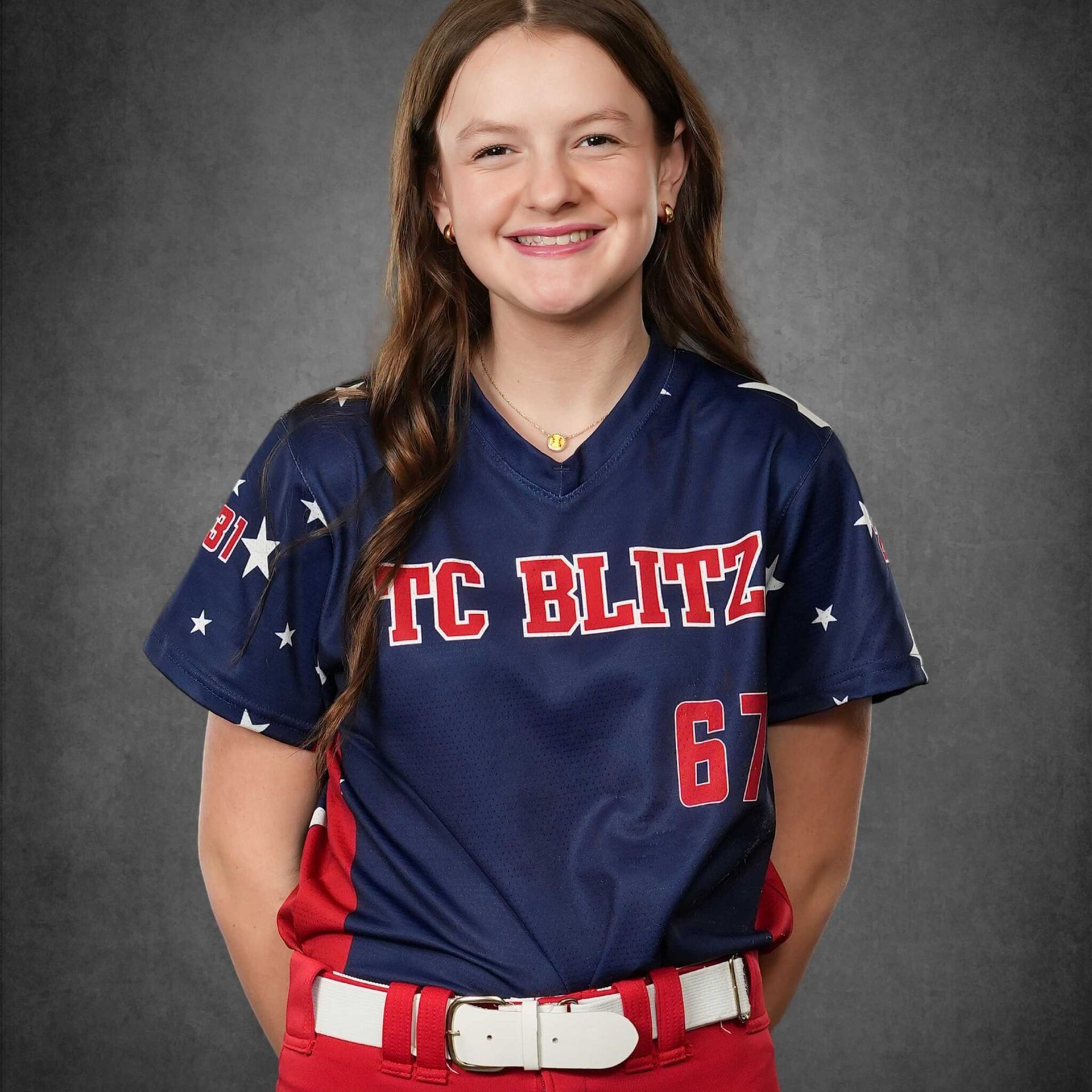 Smiling softball player in navy and red TC BLITZ uniform against a gray backdrop