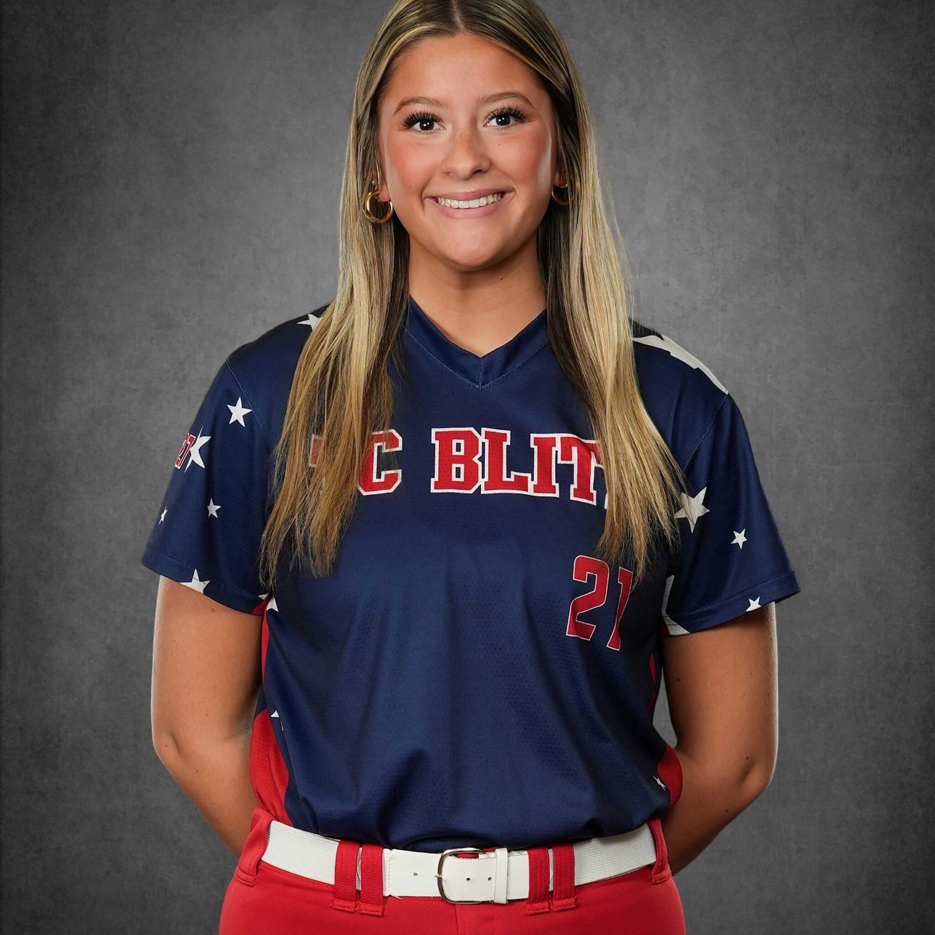 Portrait of a smiling baseball player in a navy jersey and red pants against a gray backdrop