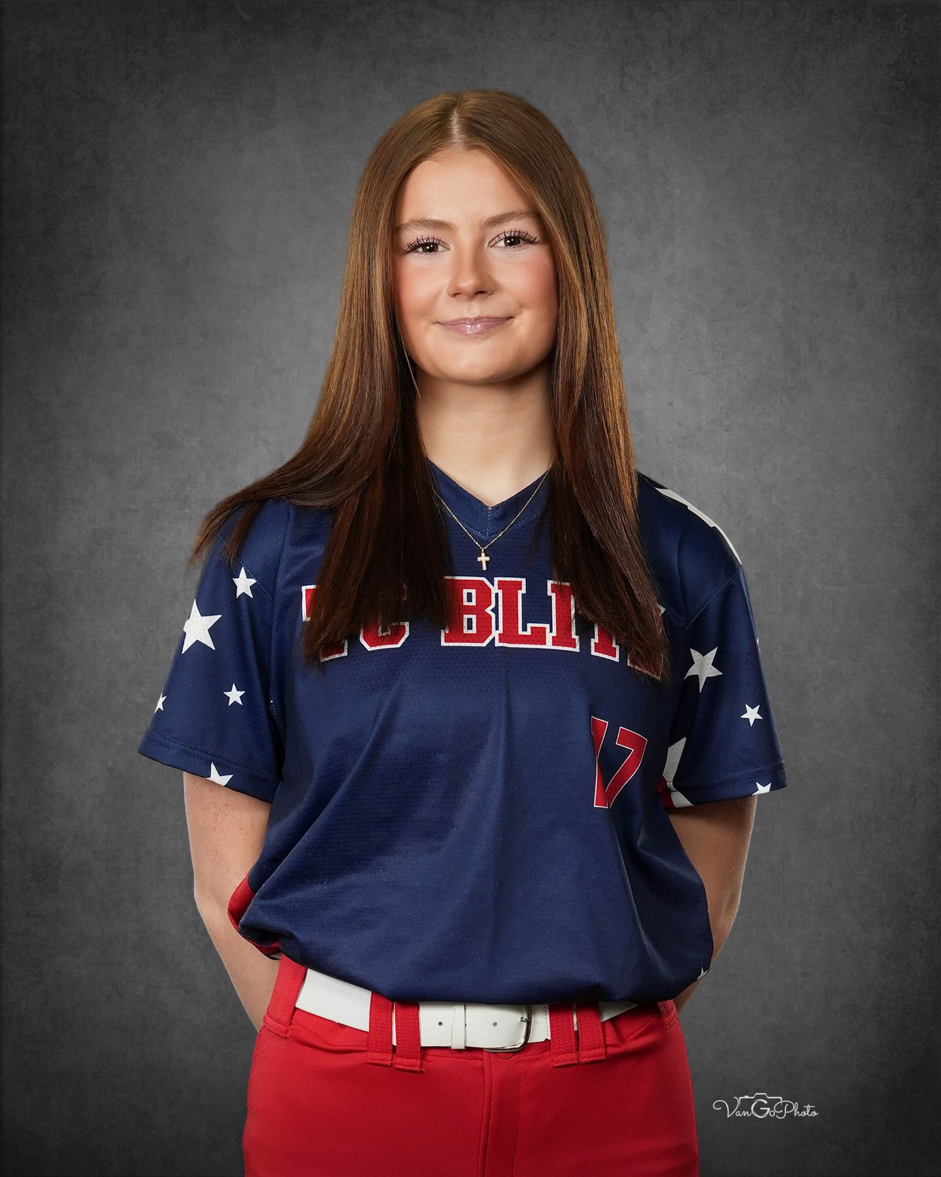 Portrait of a person in a navy and red sports jersey, standing against a gray studio backdrop.
