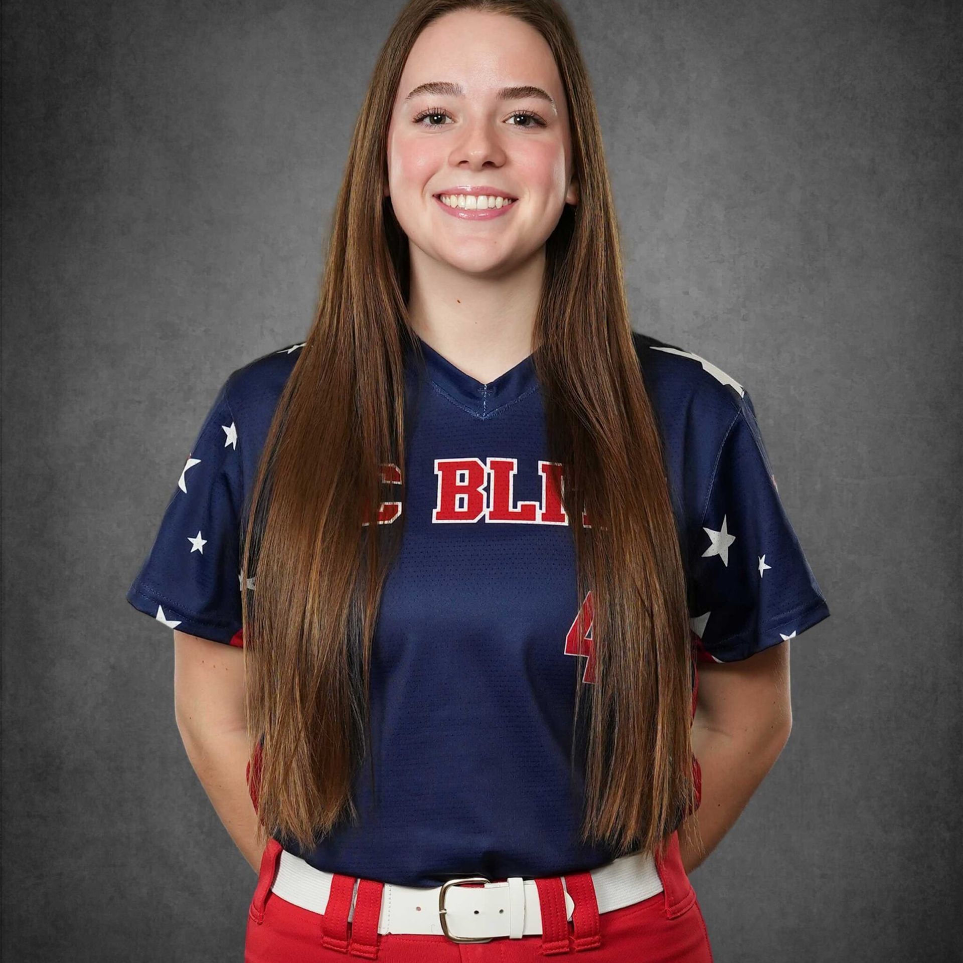 Woman in a navy and red softball uniform, smiling against a gray studio backdrop.