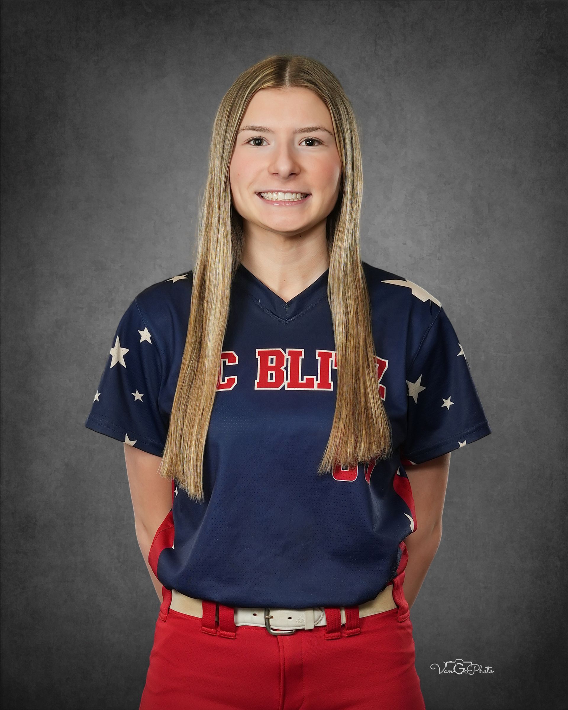Smiling athlete in navy and red uniform with hands behind her back against a gray studio backdrop