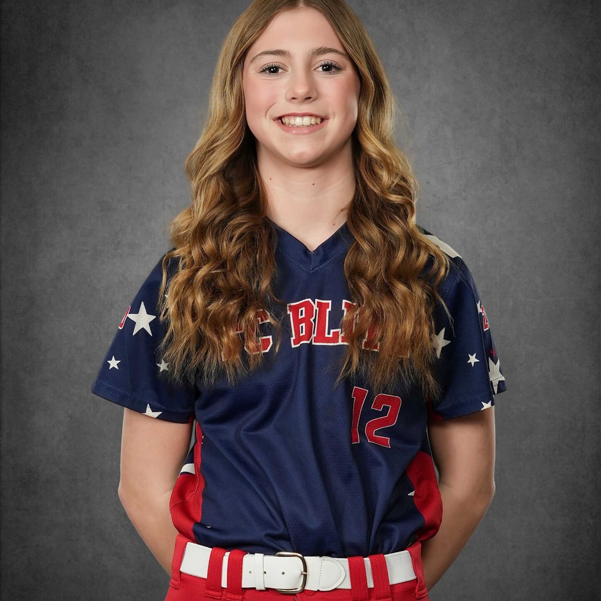 Portrait of a smiling softball player in a navy jersey and red belt against a gray backdrop