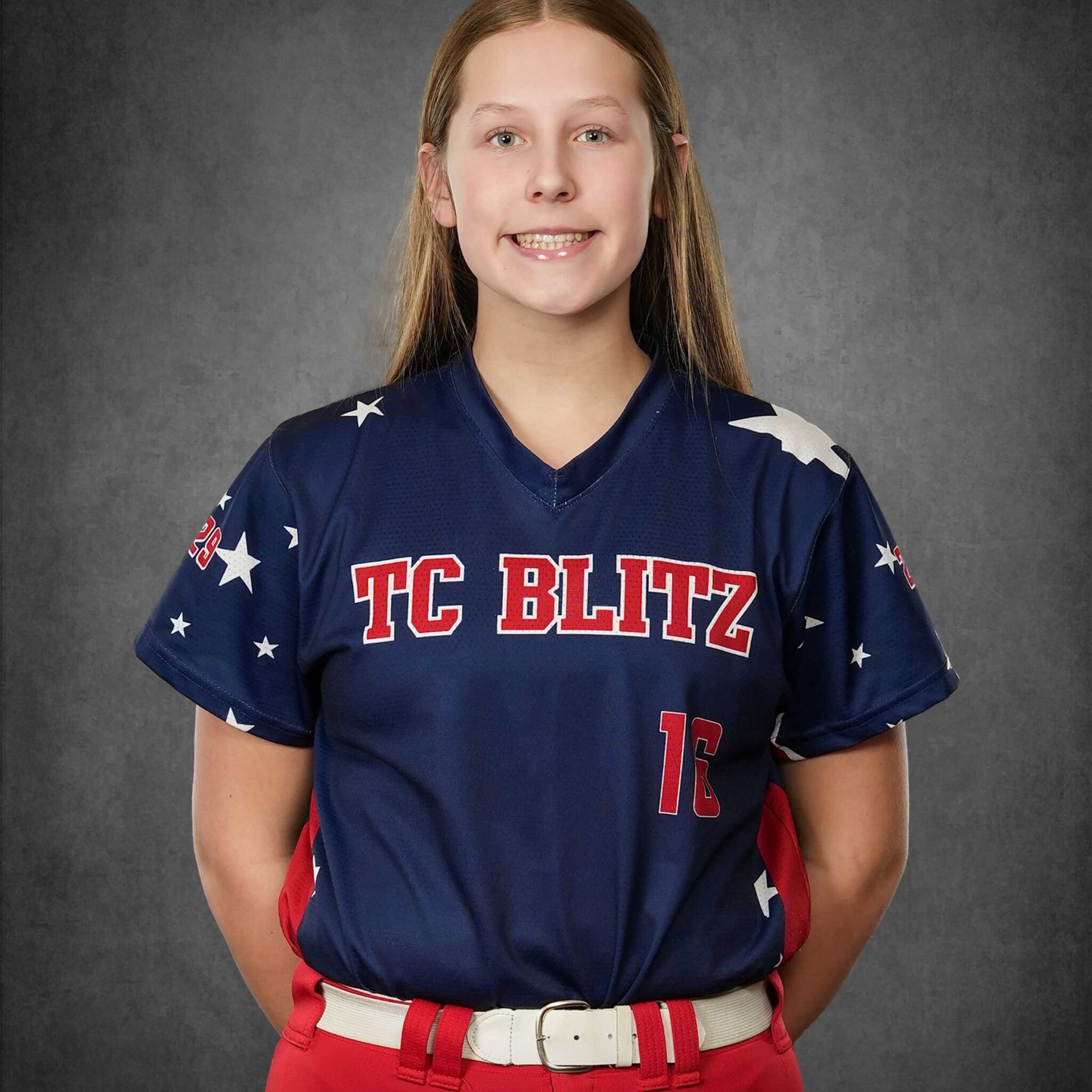 Youth softball player in blue TC Blitz jersey and red belt, standing against a gray studio backdrop.