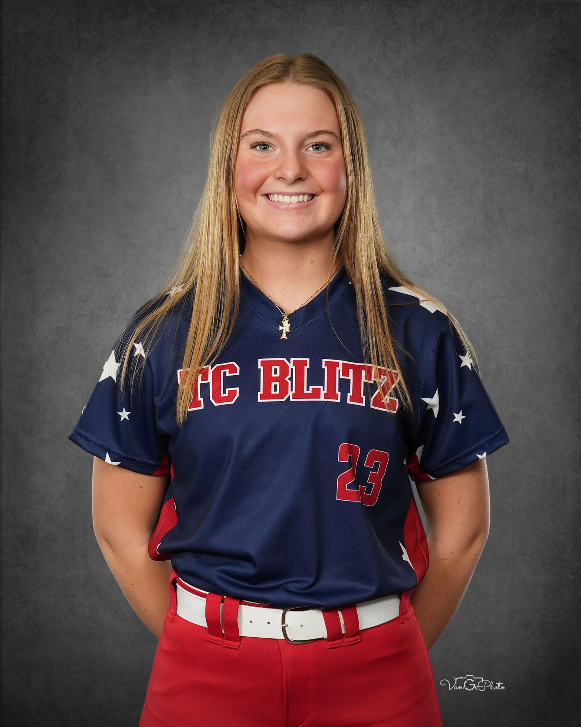 Smiling softball player in navy and red uniform against a gray studio backdrop.