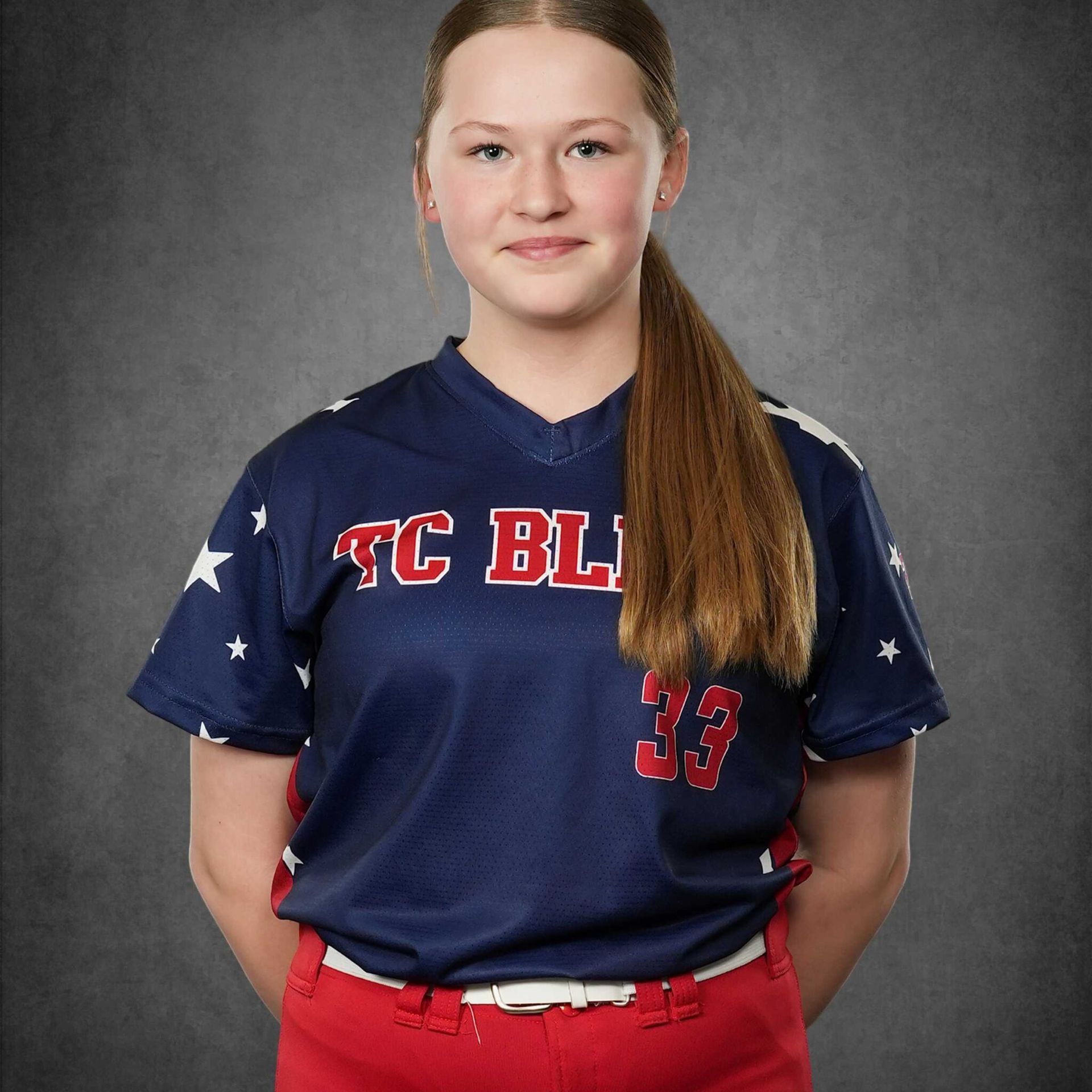 Girl in navy and red softball uniform posing against a gray studio backdrop.