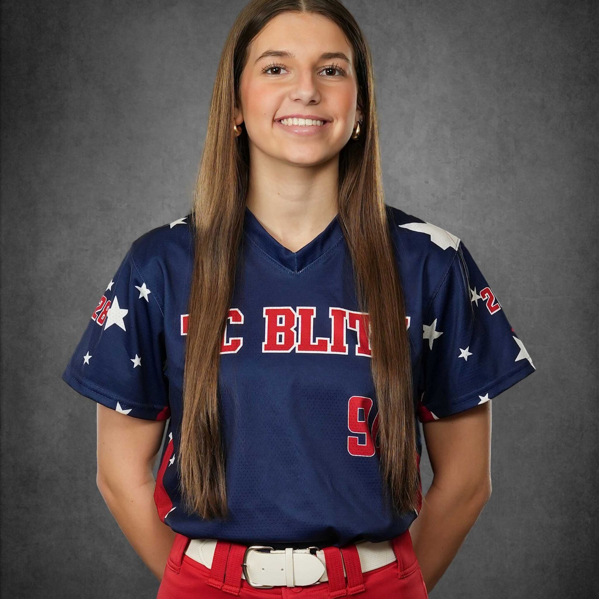 Studio portrait of a smiling athlete in a navy USA softball jersey and red pants, holding hands behind back
