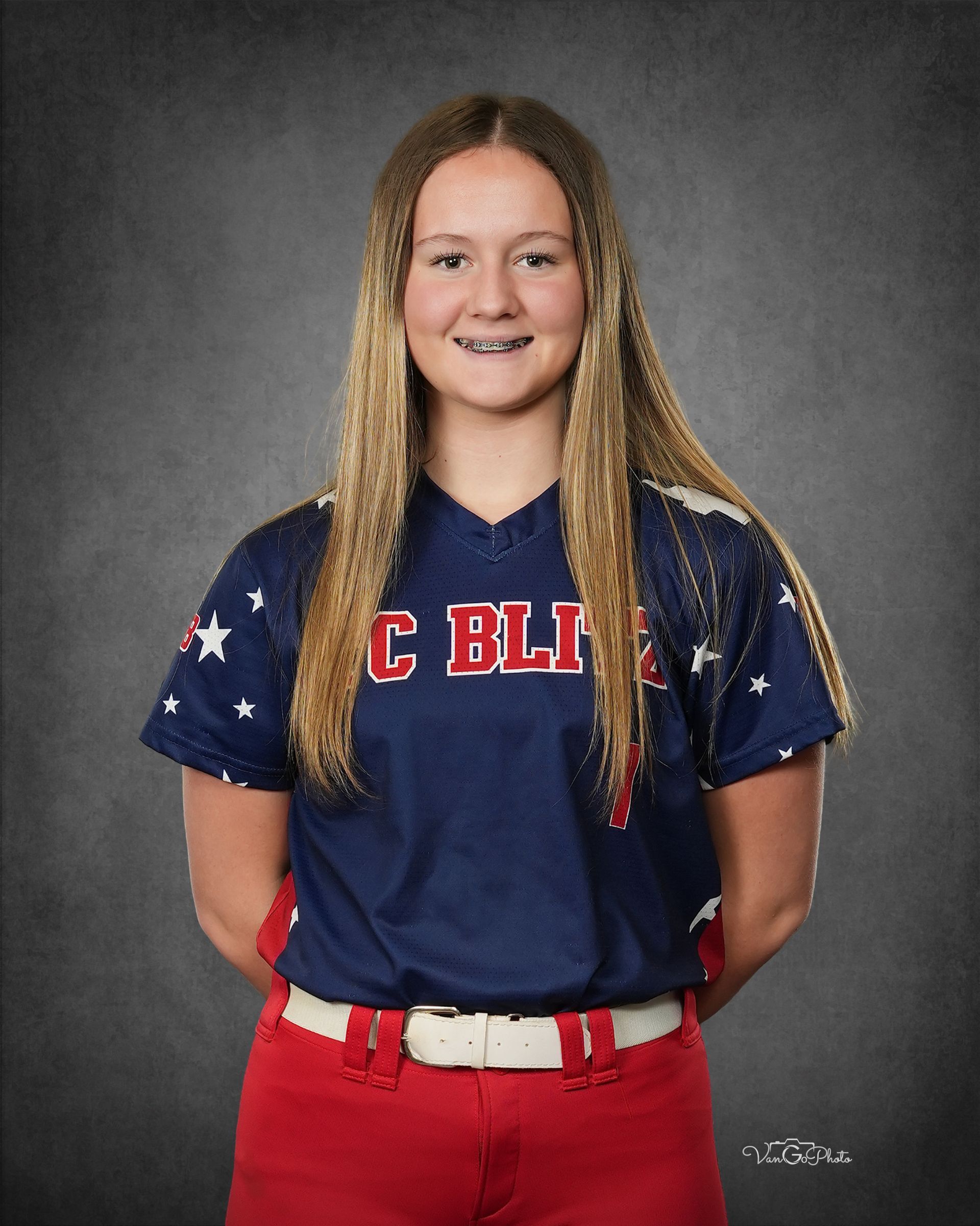 Person in a navy and red baseball uniform, smiling in a studio portrait.