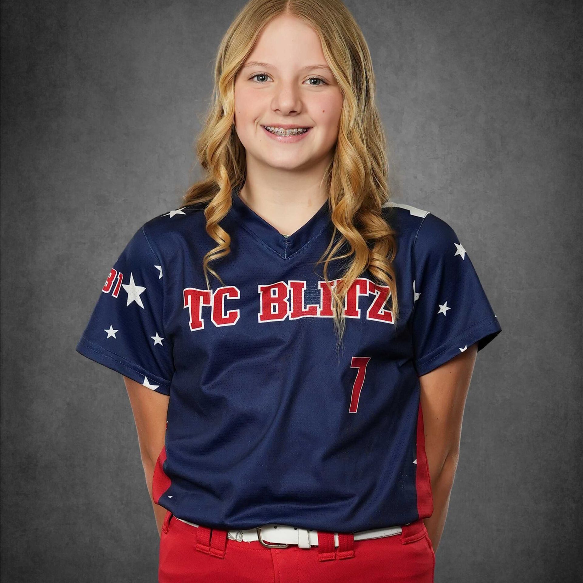 Youth softball player in navy TC Blitz jersey, smiling against a gray studio backdrop.