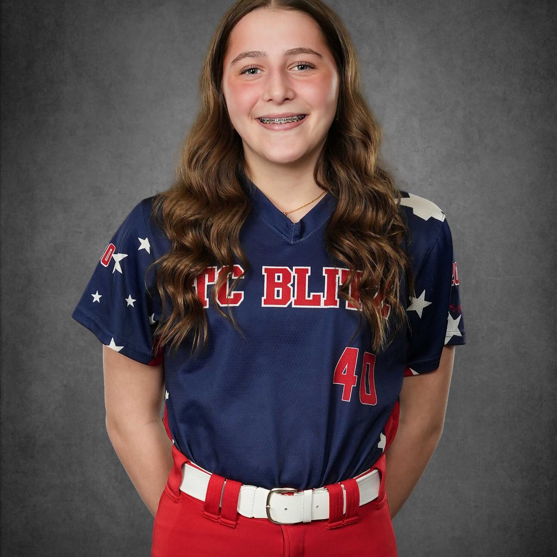 Smiling softball player in navy jersey and red pants against a gray studio backdrop
