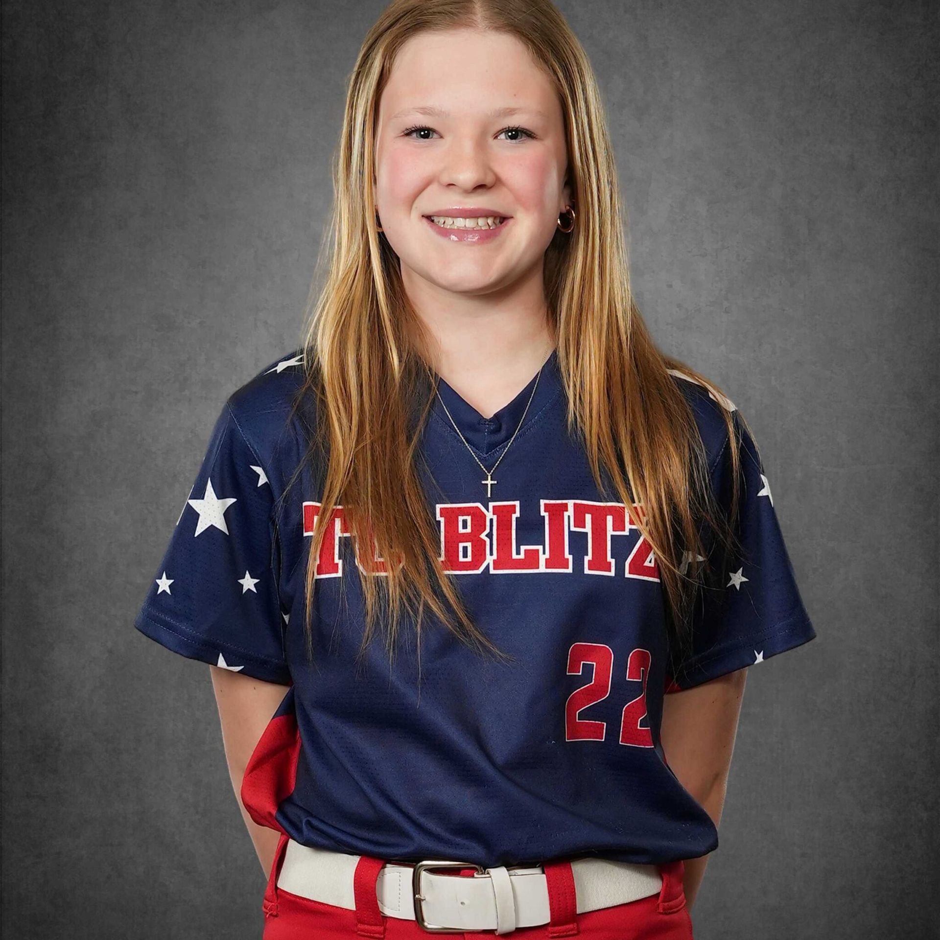 Smiling softball player in navy jersey and red belt against a gray studio backdrop