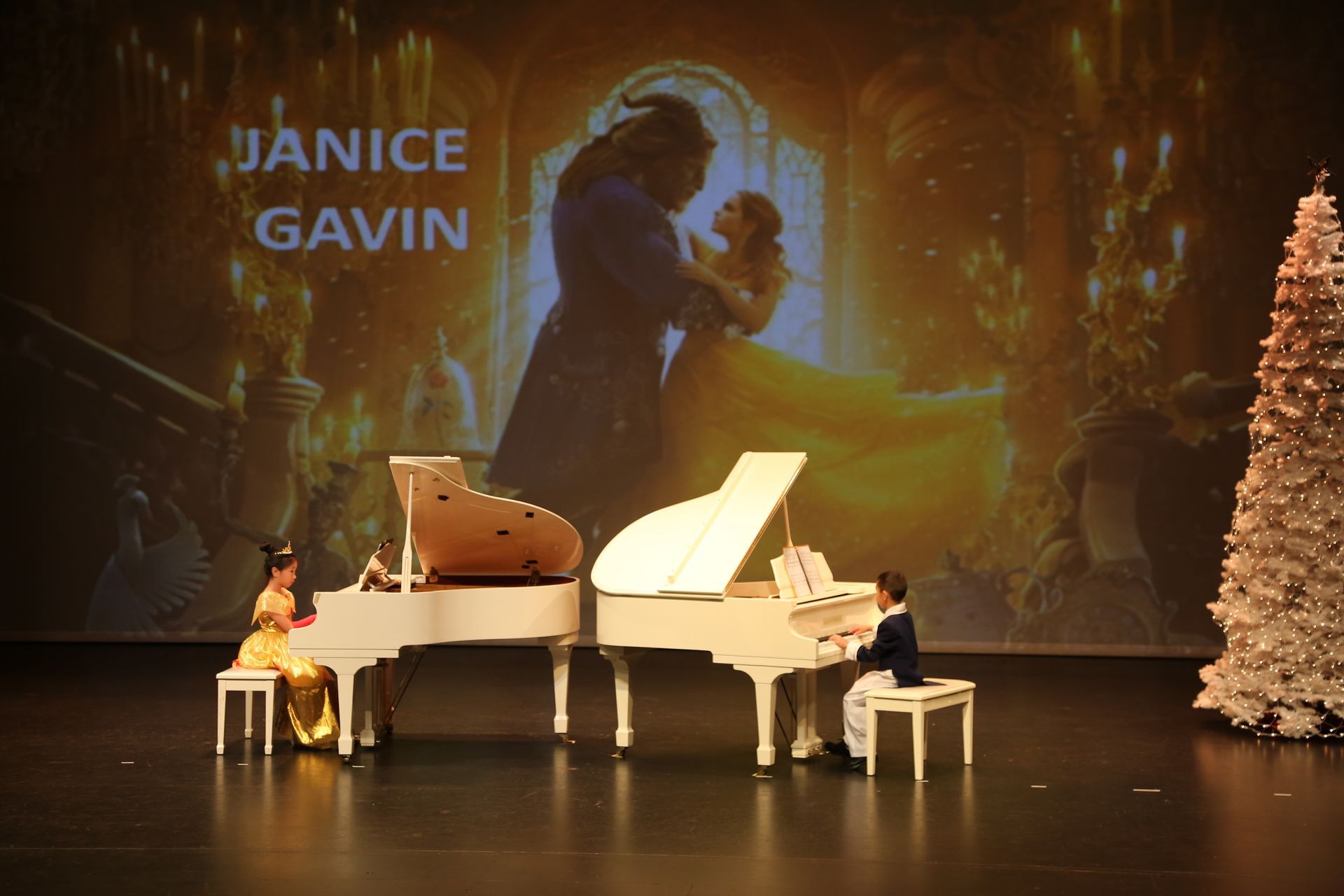Two pianists at white pianos on stage, Beauty and the Beast backdrop, Janice/Gavin text.