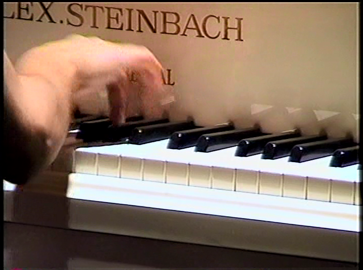 A hand plays a white piano, pressing down on the black and white keys. The piano's brand name
