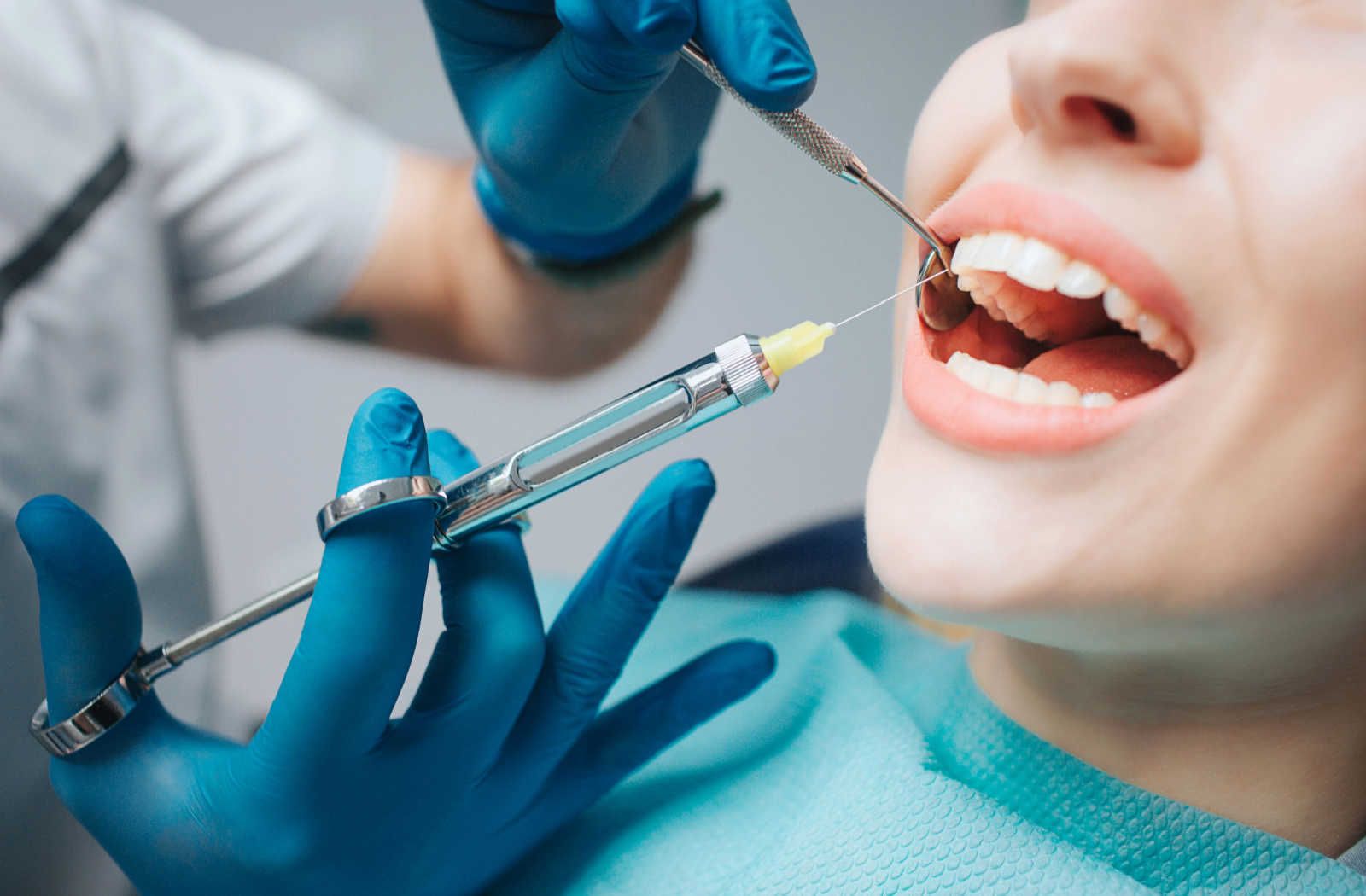 Dentist giving a patient a dental injection. Patient's mouth open, blue gloves, dental tools visible.