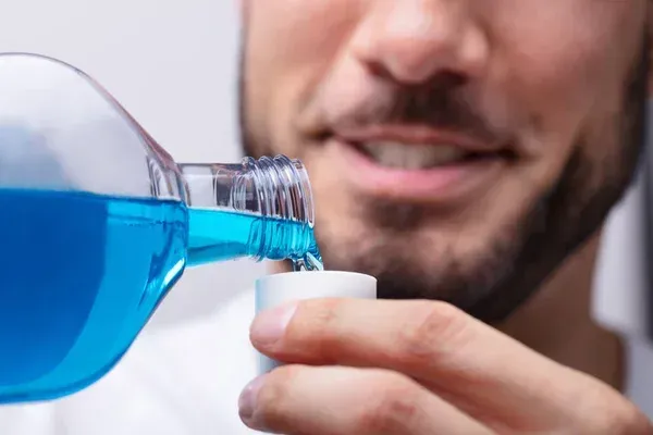 Man pouring blue mouthwash into a small cup.