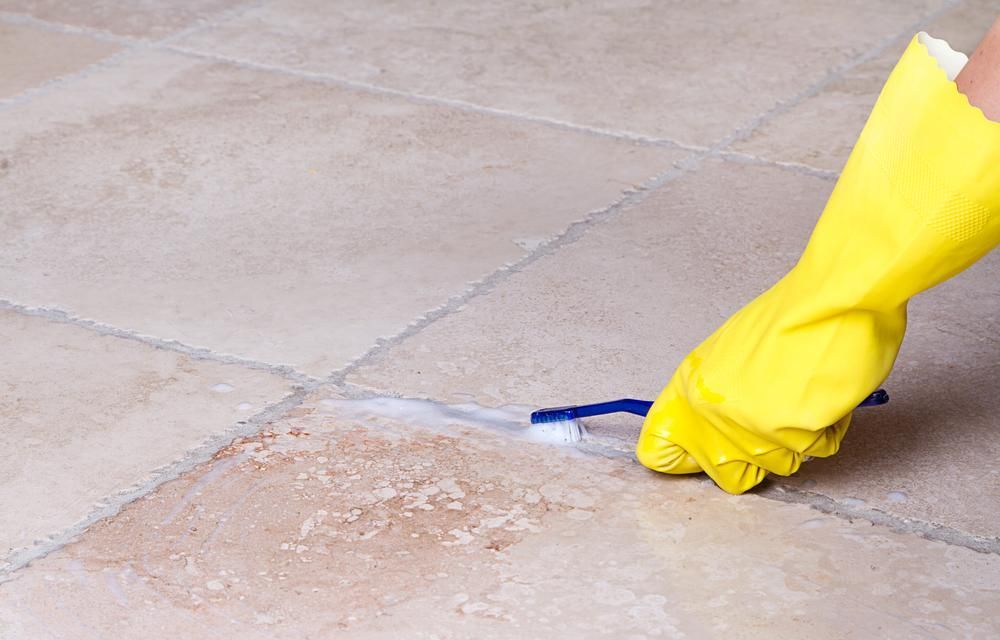 Person Wearing Yellow Gloves is Cleaning a Tile Floor With a Toothbrush — Capital Ultimate Facility in Beard, ACT