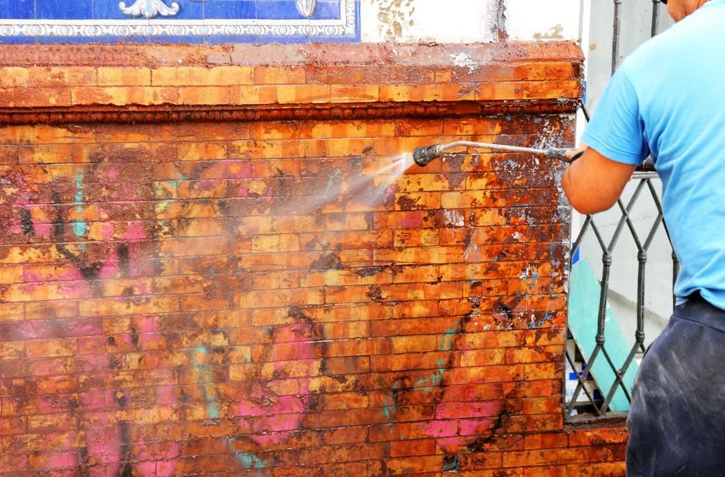 Man is Cleaning a Brick Wall With a High Pressure Washer — Capital Ultimate Facility in Queanbeyan, NSW
