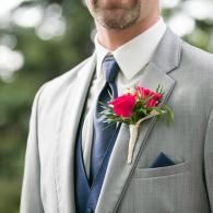 Man in a light gray suit with a blue tie and red boutonniere outdoors
