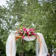 Floral wedding arch draped with white fabric under green trees
