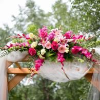 Pink and white floral arrangement draped over a wooden arch outdoors