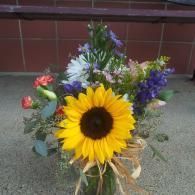 Sunflower bouquet with mixed purple, pink, and white flowers in a clear glass vase on the ground
