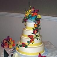 Five-tier white wedding cake with colorful flowers and ribbon accents on a table