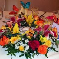 Bright mixed bouquet of roses, lilies, and daisies with butterfly decorations on a table