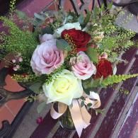 Bouquet of red, pink, and white roses with greenery and a ribbon on a patterned chair