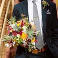 Man in dark suit holding a colorful bouquet at a wedding ceremony