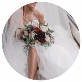 Bride in a white wedding dress holding a dark red and green bouquet.