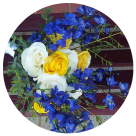 White, yellow, and blue flowers arranged in a bouquet against a dark wooden background