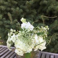 White floral bouquet on a wooden deck with evergreen trees in the background
