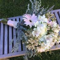 Bouquet of white and pale pink flowers resting on a gray slatted bench over grass