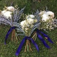 Three white and lavender floral bouquets tied with purple ribbons on grass