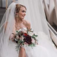 Bride in a white veil holding a bouquet of red and white flowers, seated on a staircase