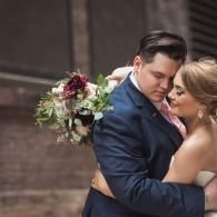 Couple embracing at a wedding, with bouquet and navy suit in soft indoor light
