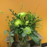 Green floral arrangement in a glass vase against an orange background