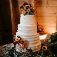 White tiered wedding cake with floral decorations on a rustic wooden table, warmly lit indoors