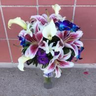 Bouquet of white, pink, and purple lilies in a clear vase against a red brick wall