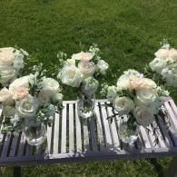 White floral arrangements on a slatted bench in a grassy outdoor setting