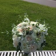 White floral bouquet with pale roses and greenery on a striped surface outdoors