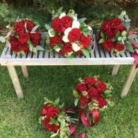 Red and white floral wreaths arranged on a small bench in a grassy outdoor setting.