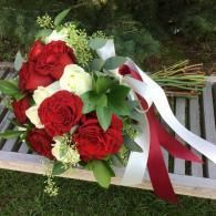 Red and white rose bouquet with green foliage and ribbon on a wooden bench outdoors