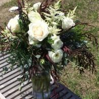White rose bouquet with greenery in a glass vase outdoors on a bench
