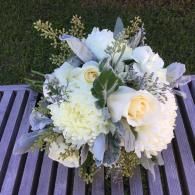 White floral bouquet with pale yellow roses and greenery on a slatted table outdoors