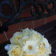 Bouquet of white and pale yellow flowers on a dark bench against a brick wall